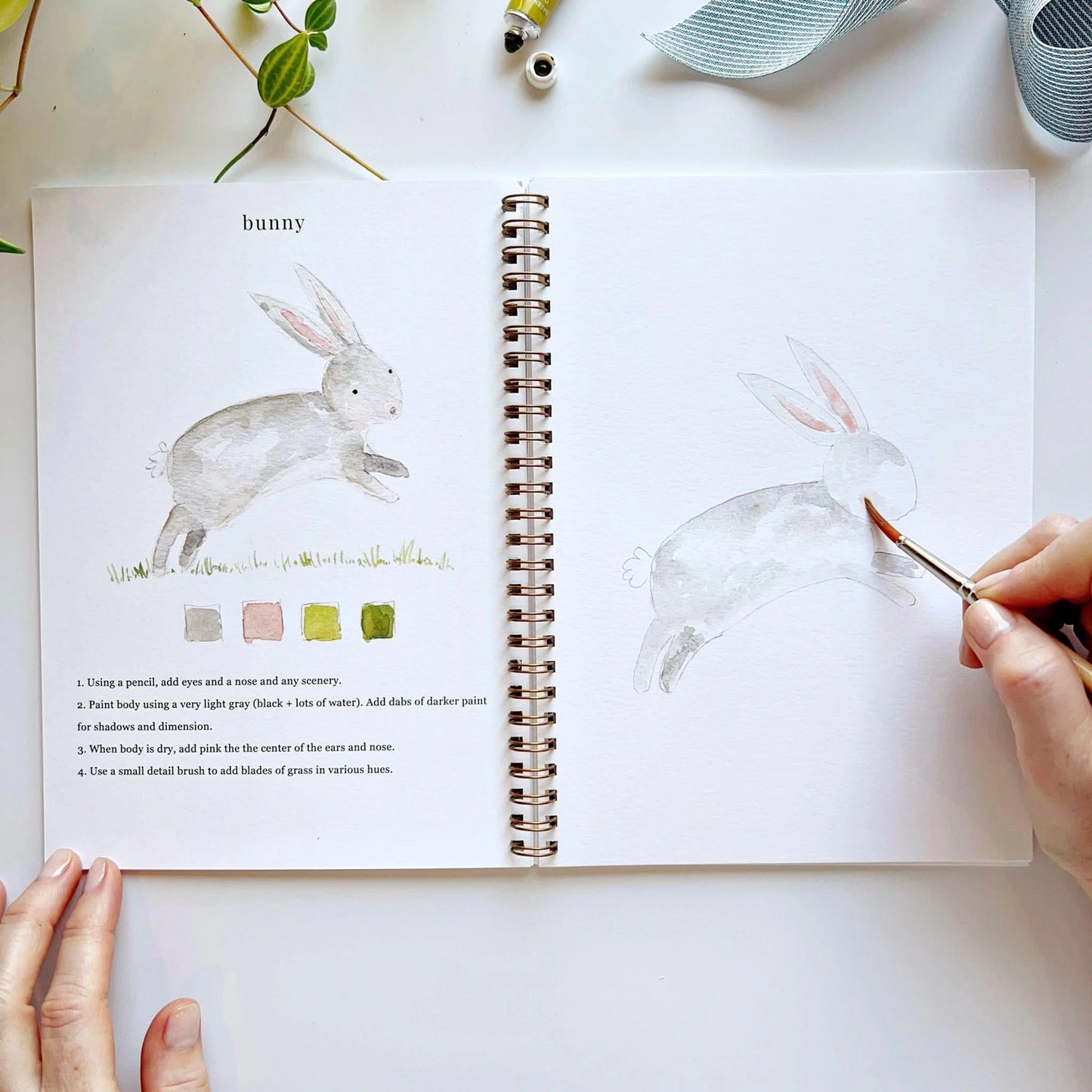 Open book with rabbit illustration and painting activity, hands holding a brush.