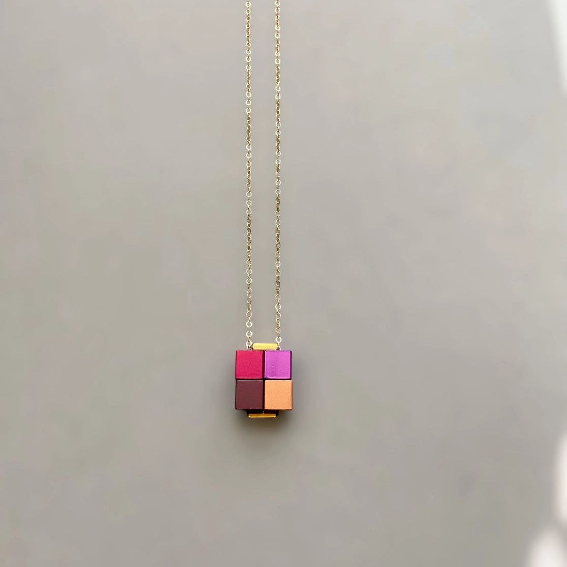 Necklace with a pink and gold cube pendant on a light gray background