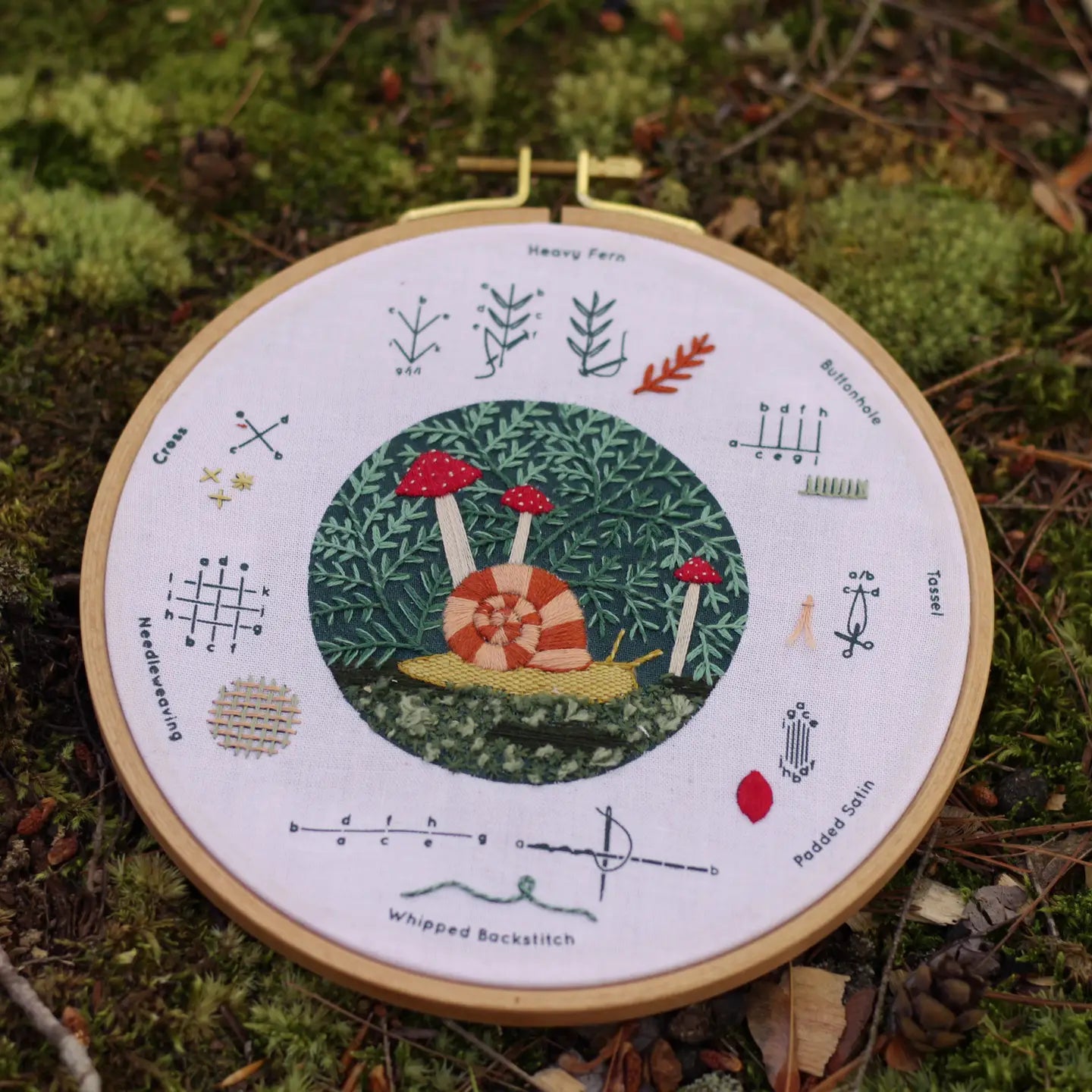 Embroidery hoop with nature-themed design on a mossy background