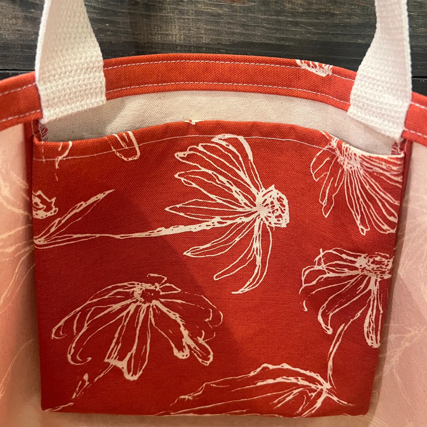 Red tote bag with white floral patterns on a wood surface