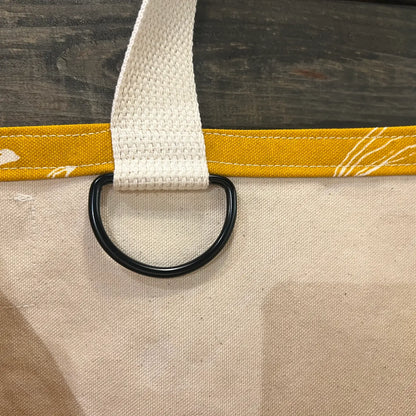 Close-up of a beige bag with a yellow strap and black ring on a wooden surface