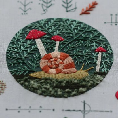Embroidered design of a snail among red mushrooms on green foliage.