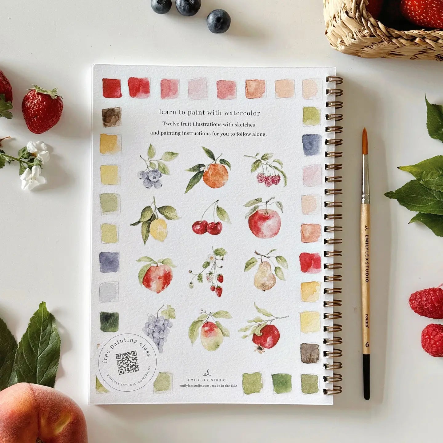 Notebook with watercolor fruit illustrations on a table with fruits and a brush