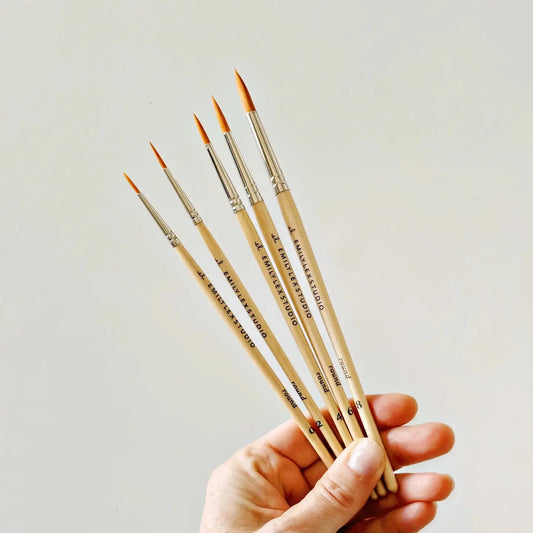 Hand holding a set of paintbrushes against an off-white background