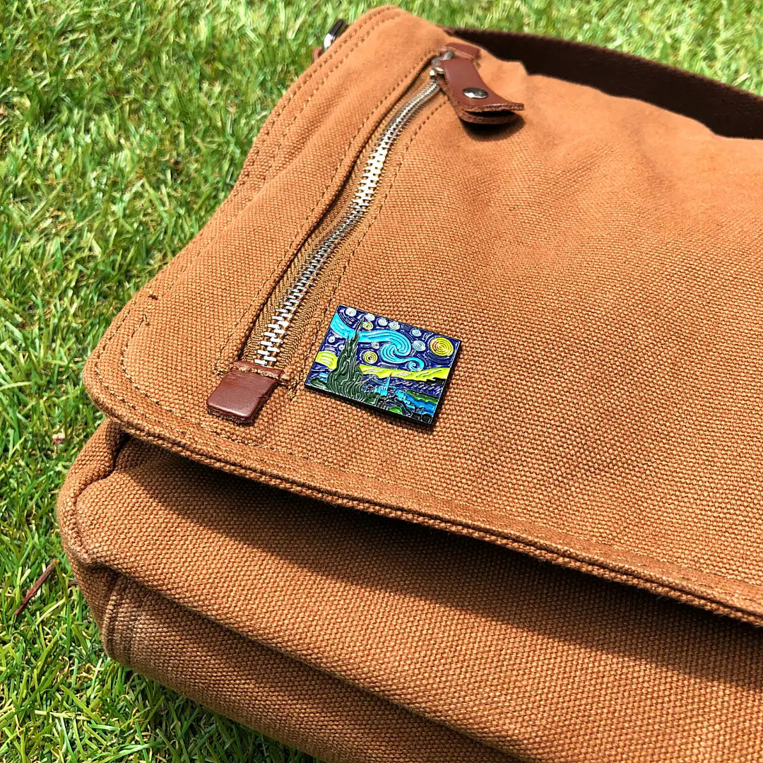Brown bag with a small Starry Night enamel pin on a grassy background