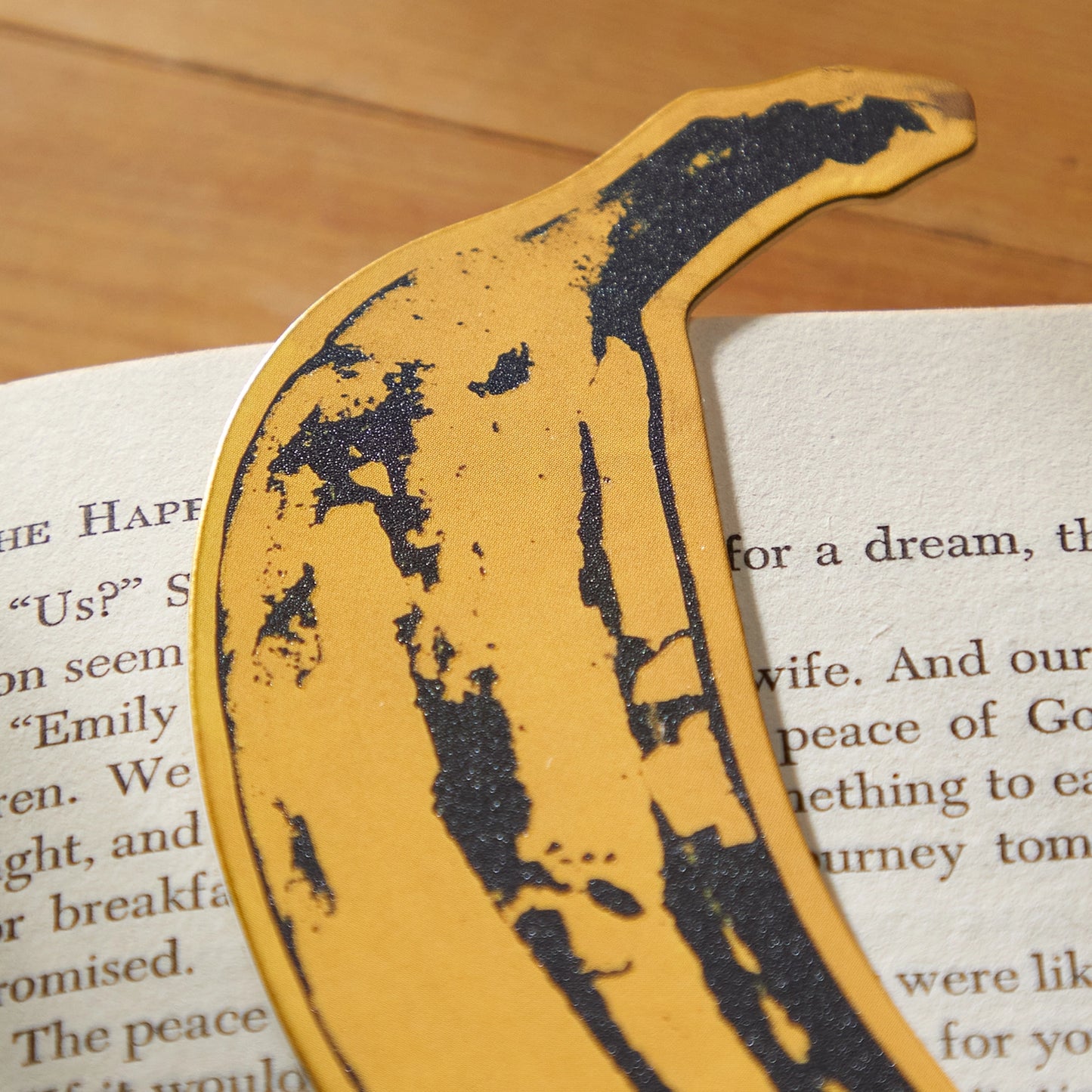 A yellow and black banana shaped bookmark laying in a book on a wood background.