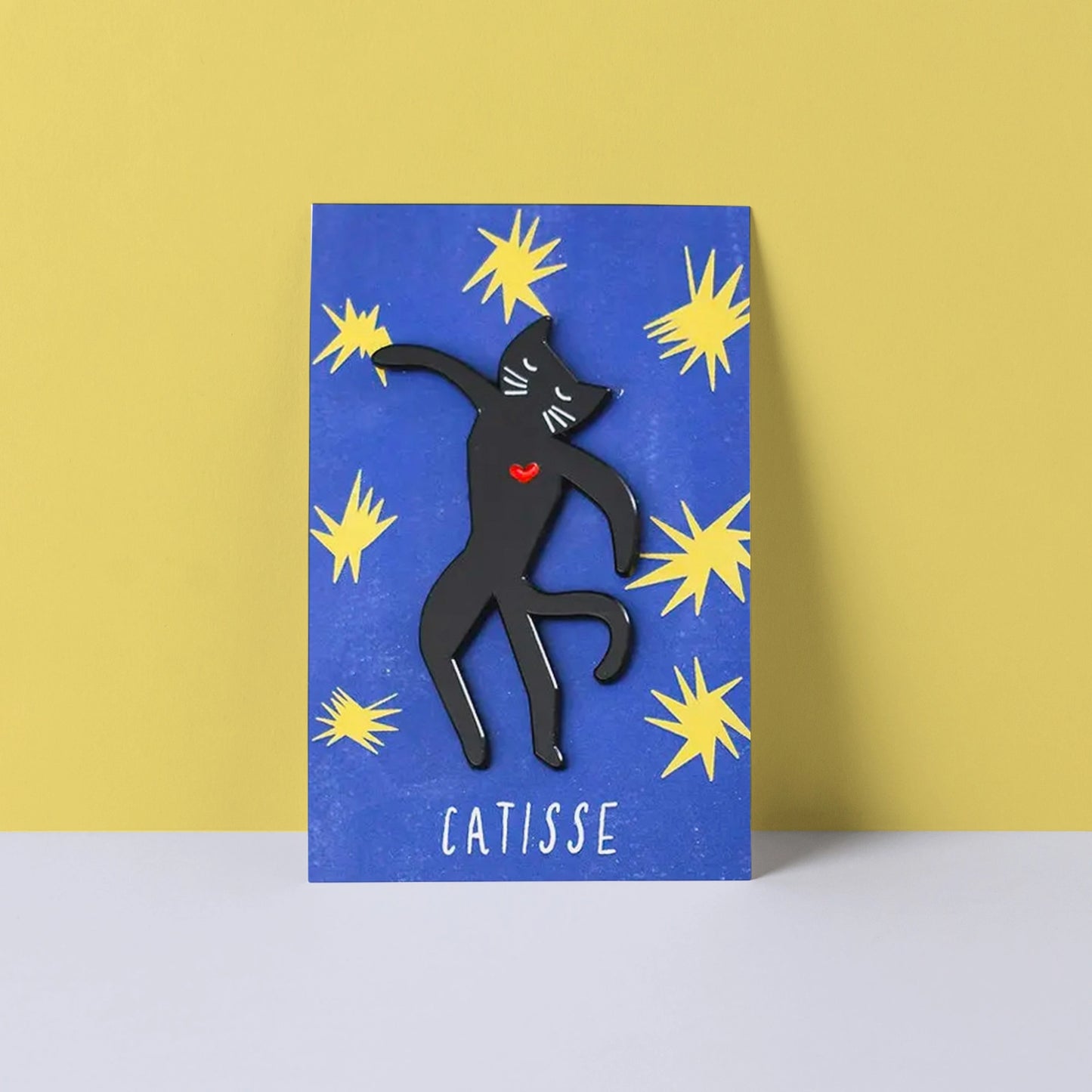 Black cat enamel pin on a blue card with yellow stars against a yellow background
