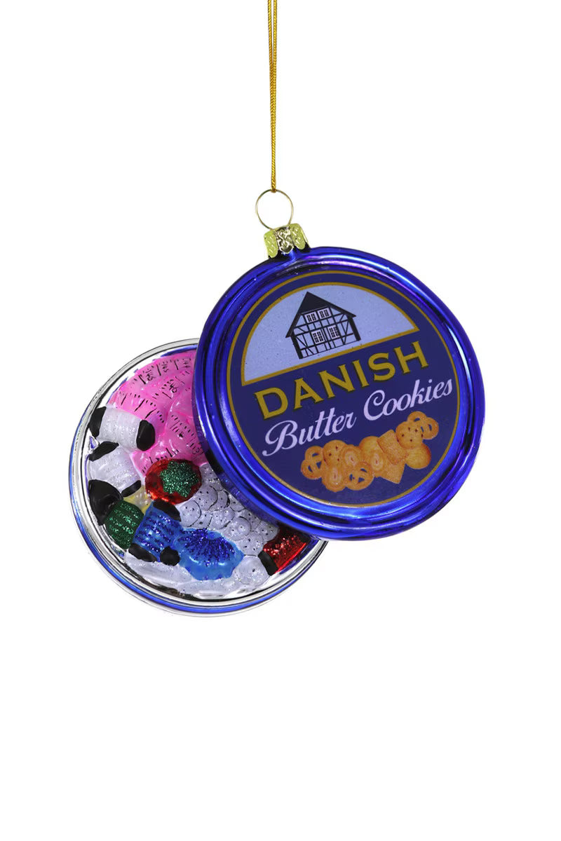 A glass Christmas ornament shaped like an open Danish Butter Cookies tin containing tread, a pink tape measure and a red pin cushion with a gold ribbon on white background