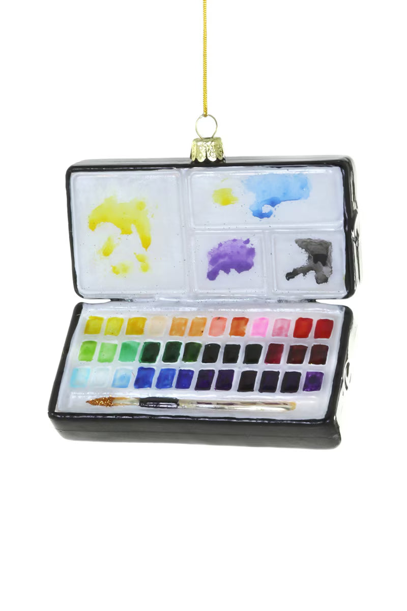 A glass ornament shaped like a watercolor set with a gold hanging cord shown on a white background.