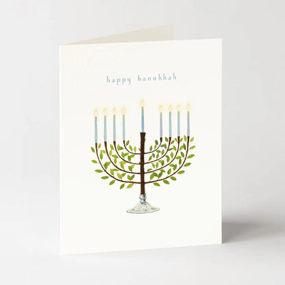 A cream card with a the words "happy hanukkah" and a watercolor image of a menorah on a light grey background