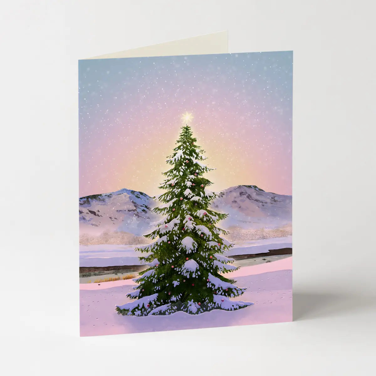 A card featuring a green Christmas tree against a pastel landscape on a light grey background
