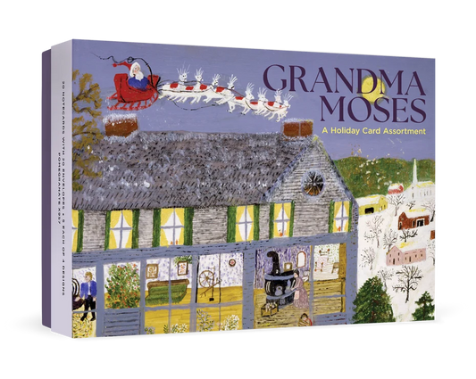 Packaging for boxed holiday notecards featuring artist Granda Moses' painting of a blue house in a snowy landscape with Santa flying overhead.