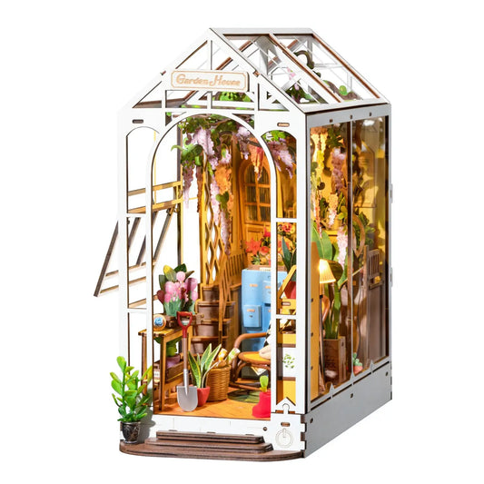 A miniature wooden greenhouse with plants and a chair inside on a white background.