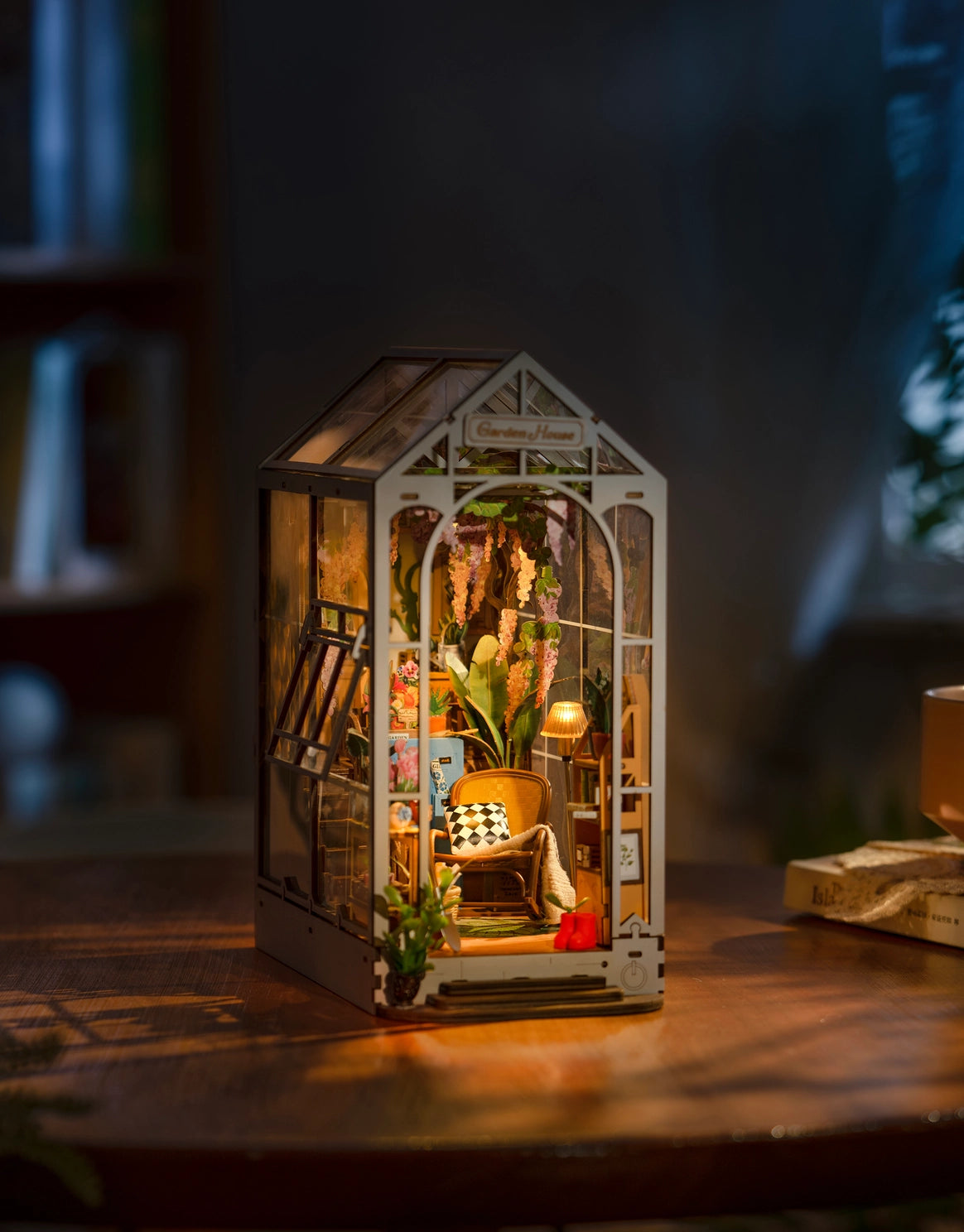 A lit miniature white greenhouse against a nighttime background
