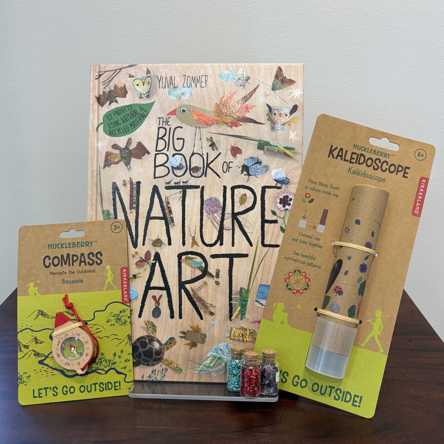 Nature-themed book and accessories including a compass, kaleidoscope, and small bottles on a wooden surface.