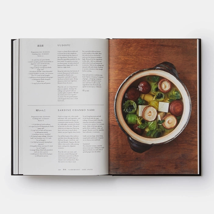 Open book with a page detailing the recipe for Sardine Chanko Nabe and an other page featuring a bowl of soup on a wooden background.
