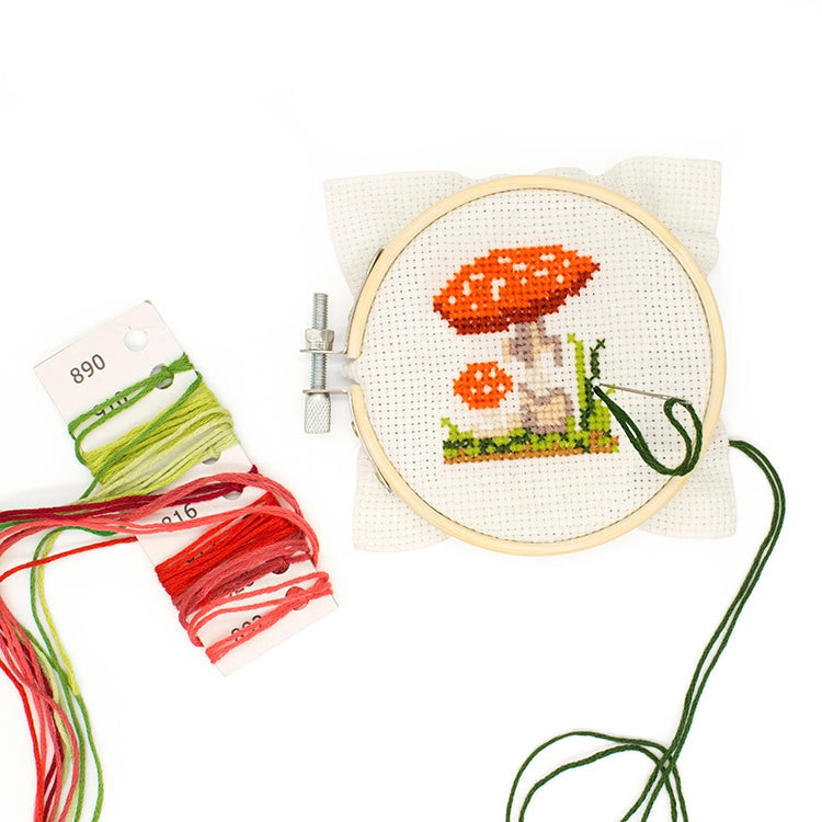 Embroidery hoop with mushroom design and colorful threads on a white background