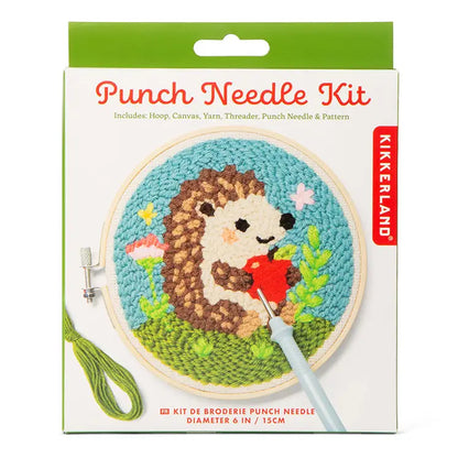 Product pakaging for a 'Punch Needle Kit'. On the front of the packaging is an image of a round wooden frame with a metal screw holding a sample of rug hooking showing a hedgehog holding an apple. All shown on a white background.