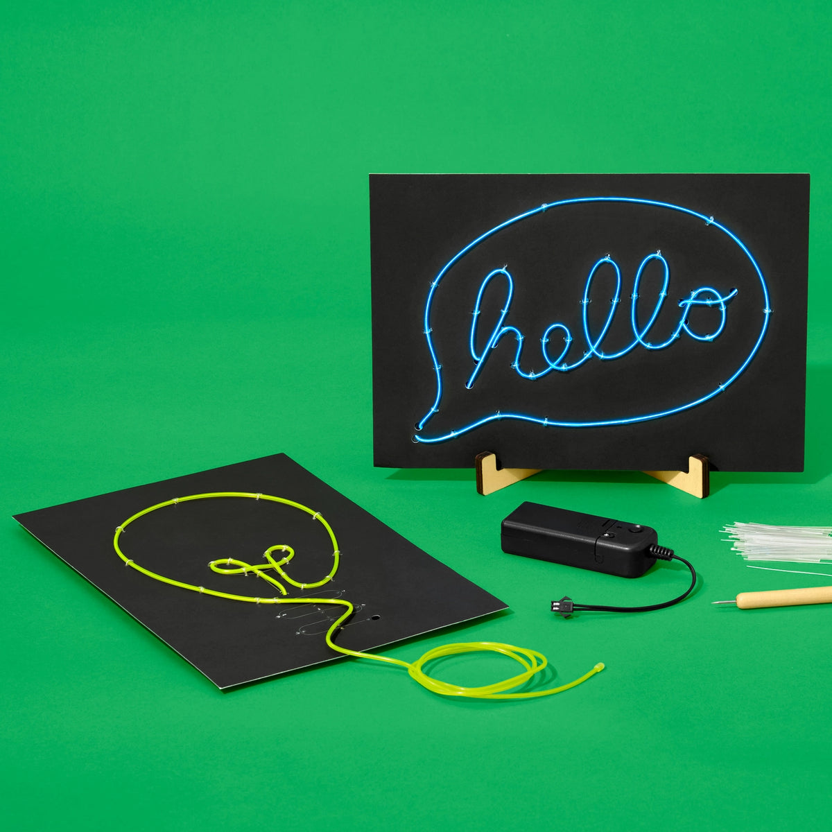 Two black wire art signs one with the word 'hello' in blue wire and one with a light bulb in yellow shown on a bright green background