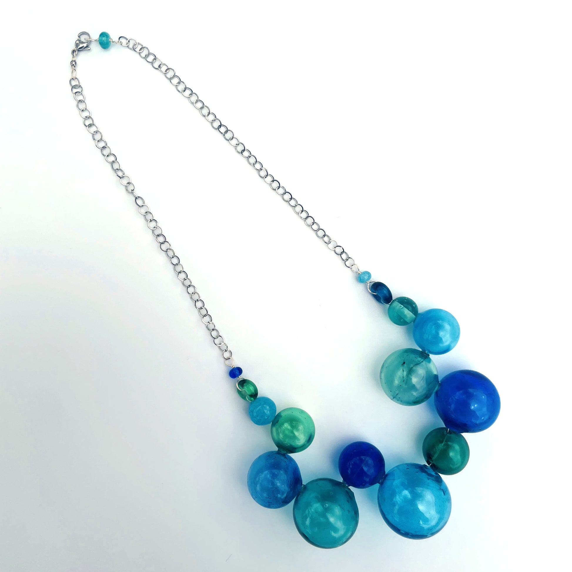 A beaded necklace with a silver chain, featuring large translucent blue and green glass beads with smaller accent beads, displayed on a white background.