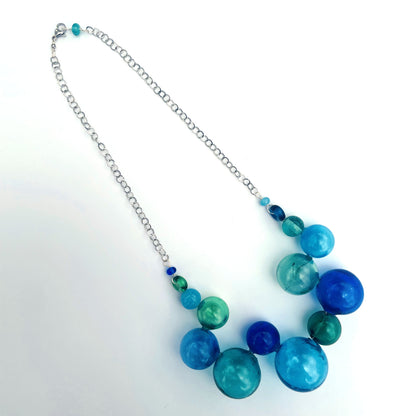A beaded necklace with a silver chain, featuring large translucent blue and green glass beads with smaller accent beads, displayed on a white background.