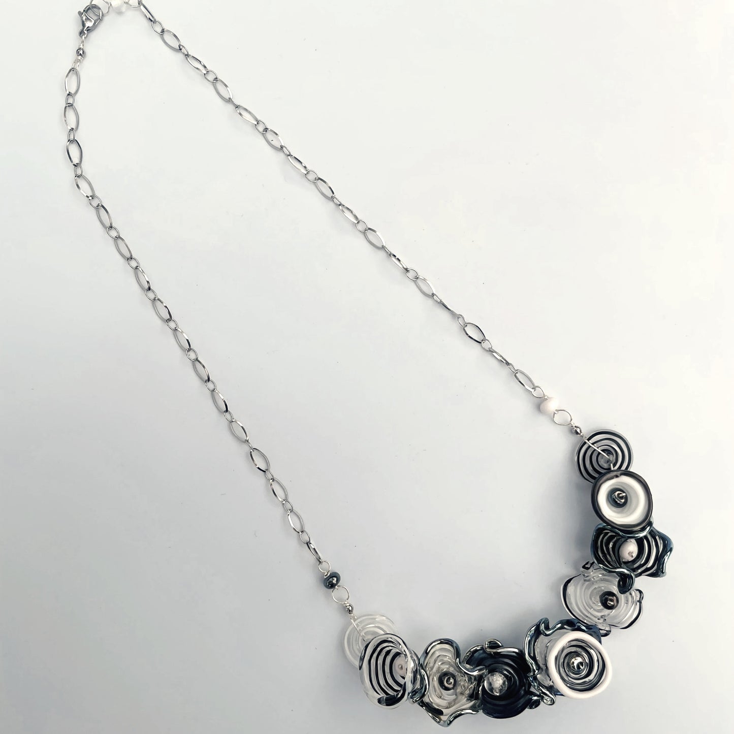 A silver chain necklace featuring a cluster of black and silver spiral flower-shaped glass beads on a plain white background.