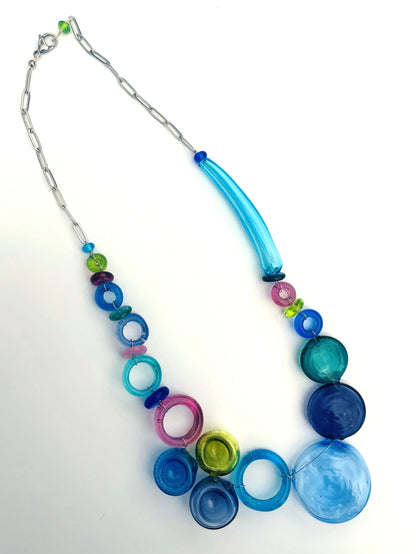 A colorful beaded necklace with a silver paperclip chain, featuring translucent blue, green, pink, and purple glass beads, including a large light blue teardrop-shaped bead, displayed on a white background..