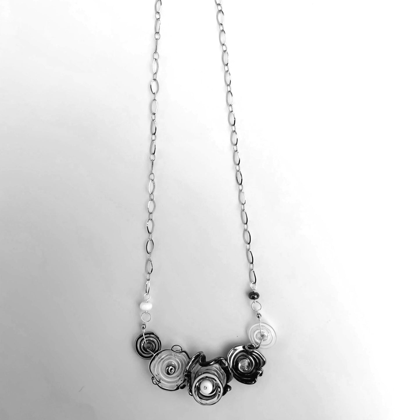 A silver-toned chain necklace featuring a cluster of black and white glass flower beads displayed against a light gray background.