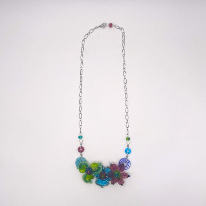 A silver chain necklace featuring a colorful cluster of glass flower charms in shades of blue, green, purple, and pink, accented with small round beads, shown against a plain white background.