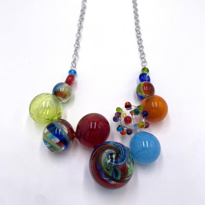 A colorful glass bead necklace with a silver chain, featuring marbled and swirled glass beads in red, blue, green, yellow, orange, and light blue on a white background.