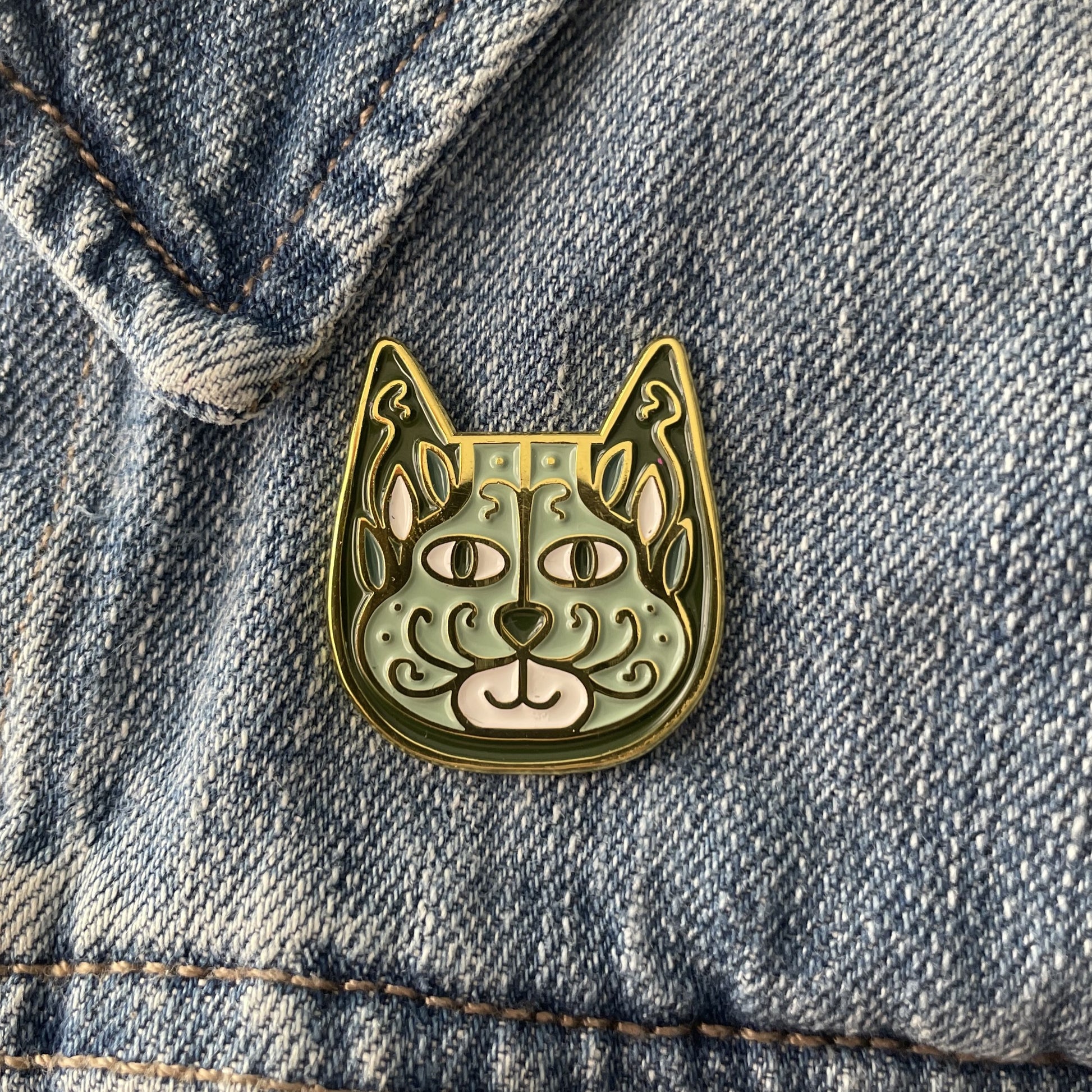 Sage green enamel cat pin on a blue jean jacket