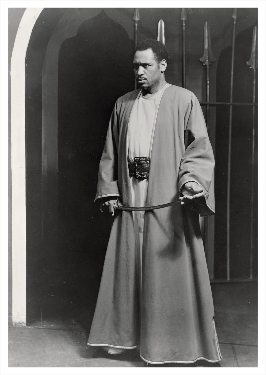Paul Robeson in a long robe holding a sword against a dark background