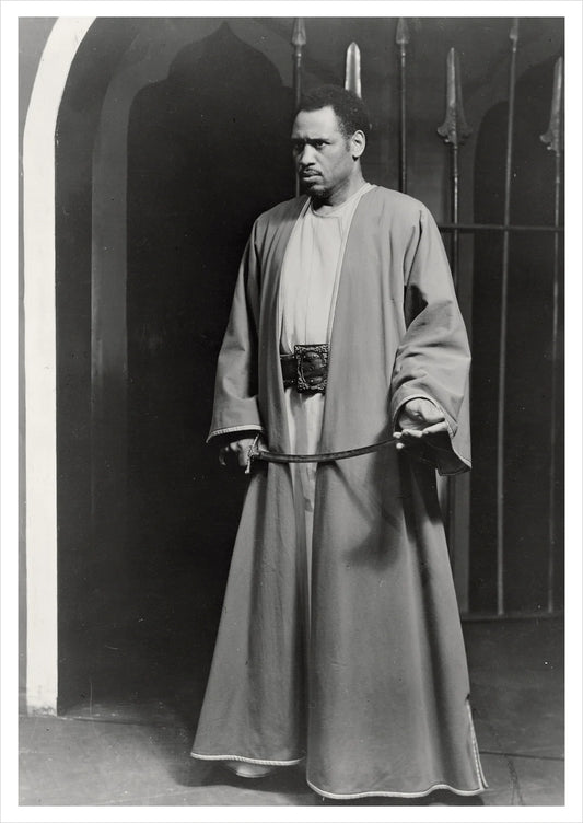 Paul Robeson in a long robe holding a sword against a dark background