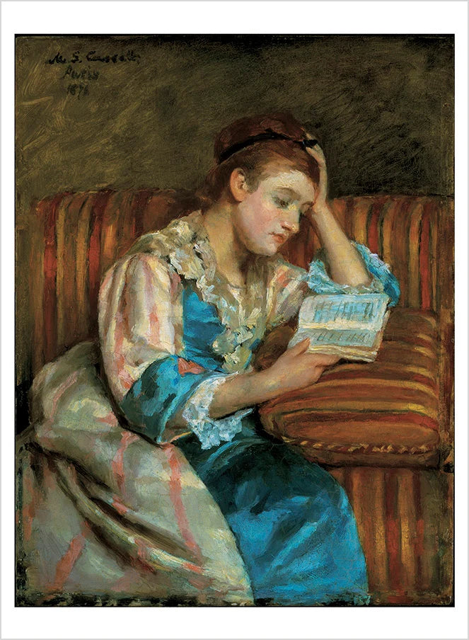 A dark haired women in a pink and blue gown seated on a striped couch reading a book
