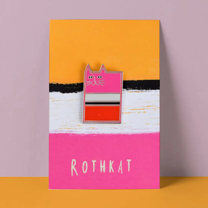 Enamel pin with a cat design on a pink card with 'ROTHKAT' text, against an orange and purple gradient background.