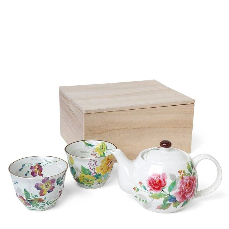 Tea set of one teapot and two tea cups with floral designs in front of a wooden box on a white background 