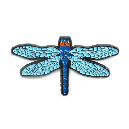 Dragonfly-shaped enamel pin with blue wings and black outline on a white background