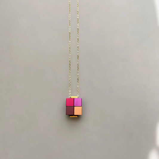 Necklace with a pink and gold cube pendant on a light gray background