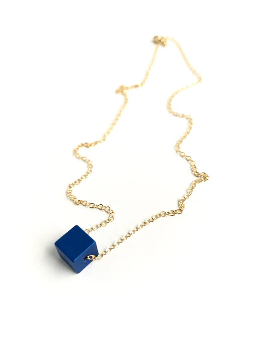 Gold necklace with a blue cube pendant on a white background