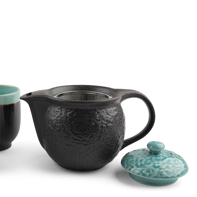 Black ceramic teapot with a textured surface, turquoise lid, and cup on a white background