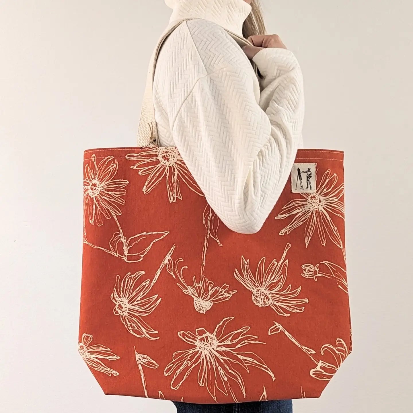 Red tote bag with floral pattern held by a person against a plain background