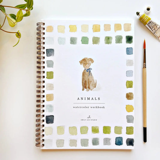 Watercolor workbook with a dog illustration on a white surface with a paintbrush and paint tube.