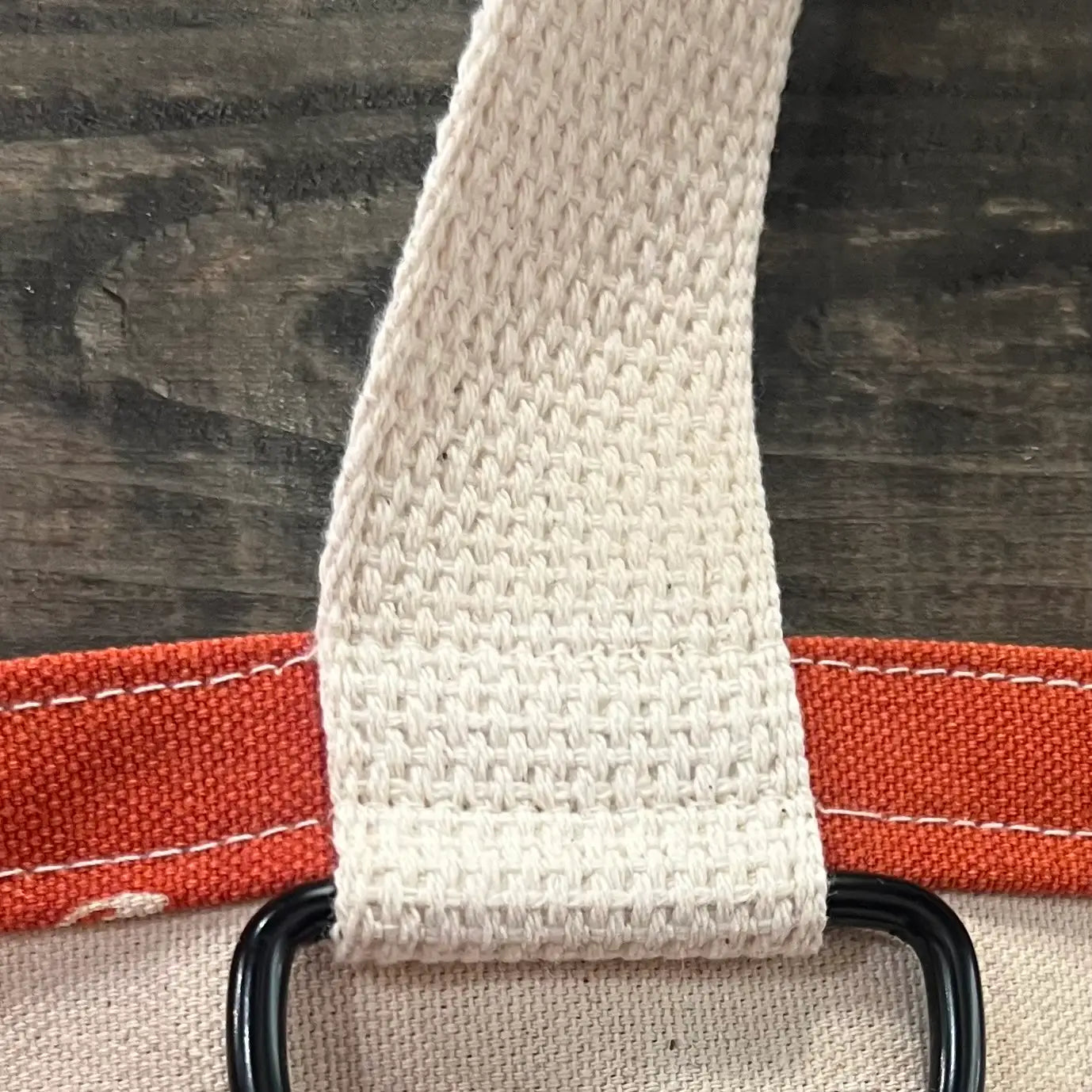 Close-up of a beige strap on a red tote bag with a black key ring on a wooden surface