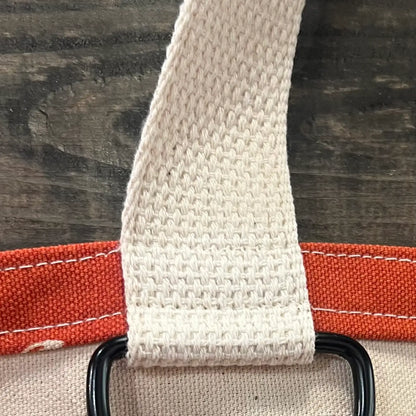 Close-up of a beige strap on a red tote bag with a black key ring on a wooden surface