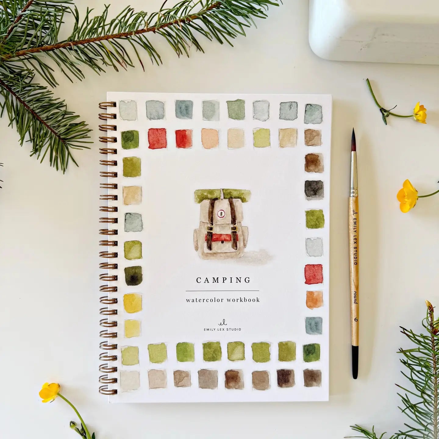Camping watercolor workbook with color swatches on a white surface with decorative elements.