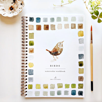 Watercolor workbook with bird illustration and color swatches on a white surface.