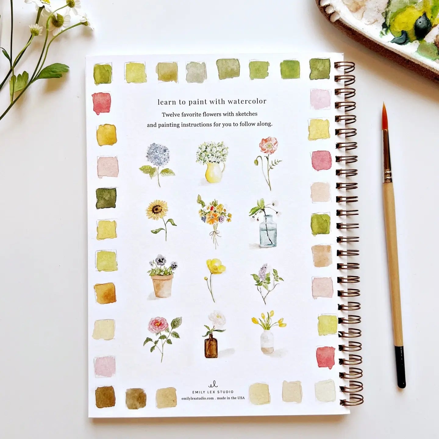 Notebook with watercolor flower illustrations and a paintbrush on a light surface
