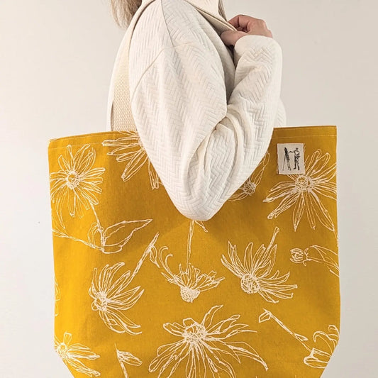 Yellow tote bag with floral pattern held by a person wearing a white coat.